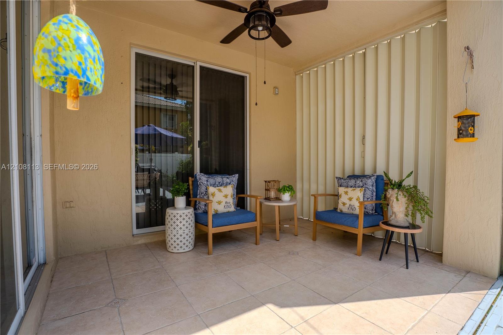 Covered patio featuring large-format tile flooring, a ceiling fan, and sliding glass entry doors with vertical blinds