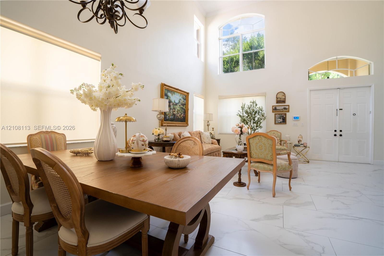 Open-concept interior featuring double-height ceilings, arched windows, large-format tile flooring, a decorative chandelier, and double-door entry