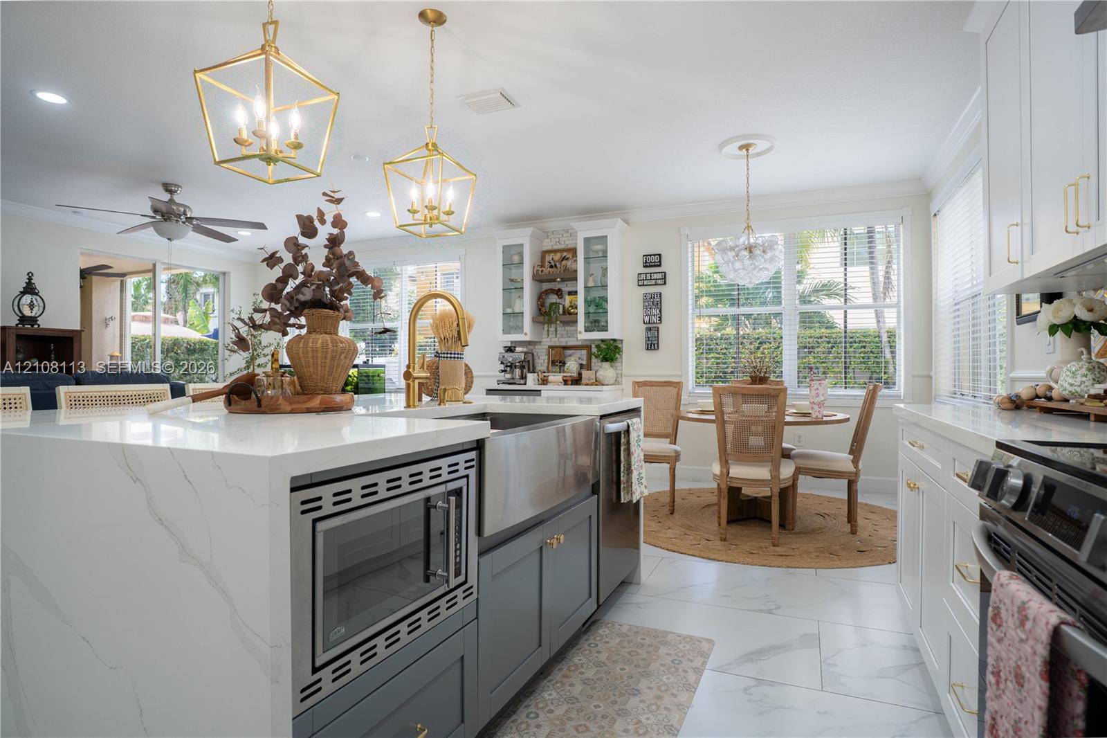 Kitchen featuring a central island with a waterfall-edge countertop, farmhouse sink, brass-finish hardware, geometric pendant lighting, and light-toned tile flooring