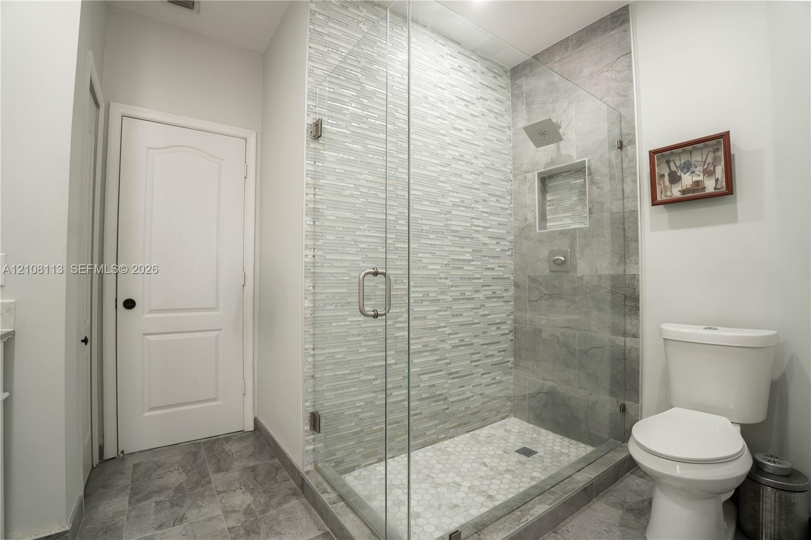 Walk-in shower featuring a frameless glass enclosure, stacked stone accent wall, inset wall niche, and hexagon tile floor