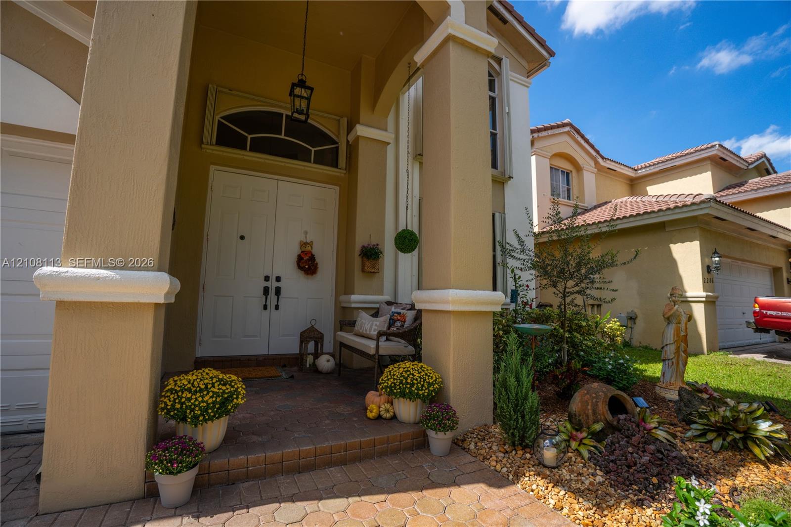 Covered entryway with double front doors, arched transom window, paver flooring, and substantial structural columns