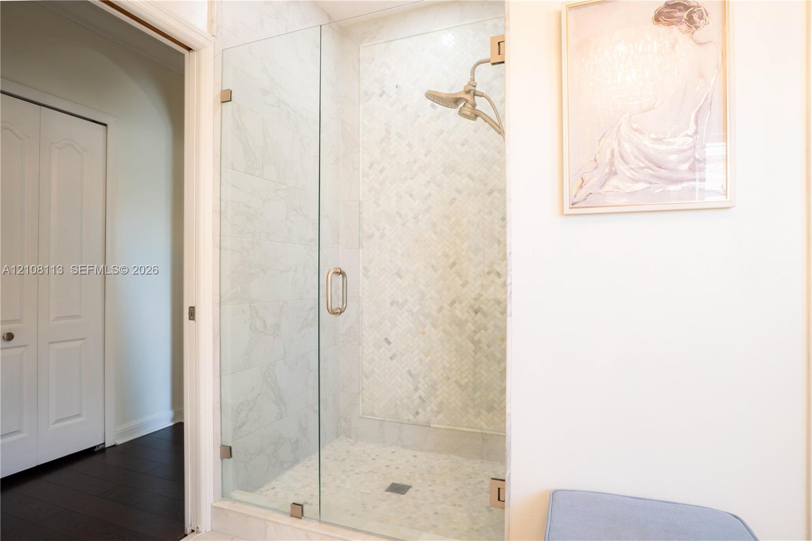 Walk-in shower featuring a frameless glass door, herringbone-patterned stone tile surround, pebble-style stone flooring, and a metallic finish shower head