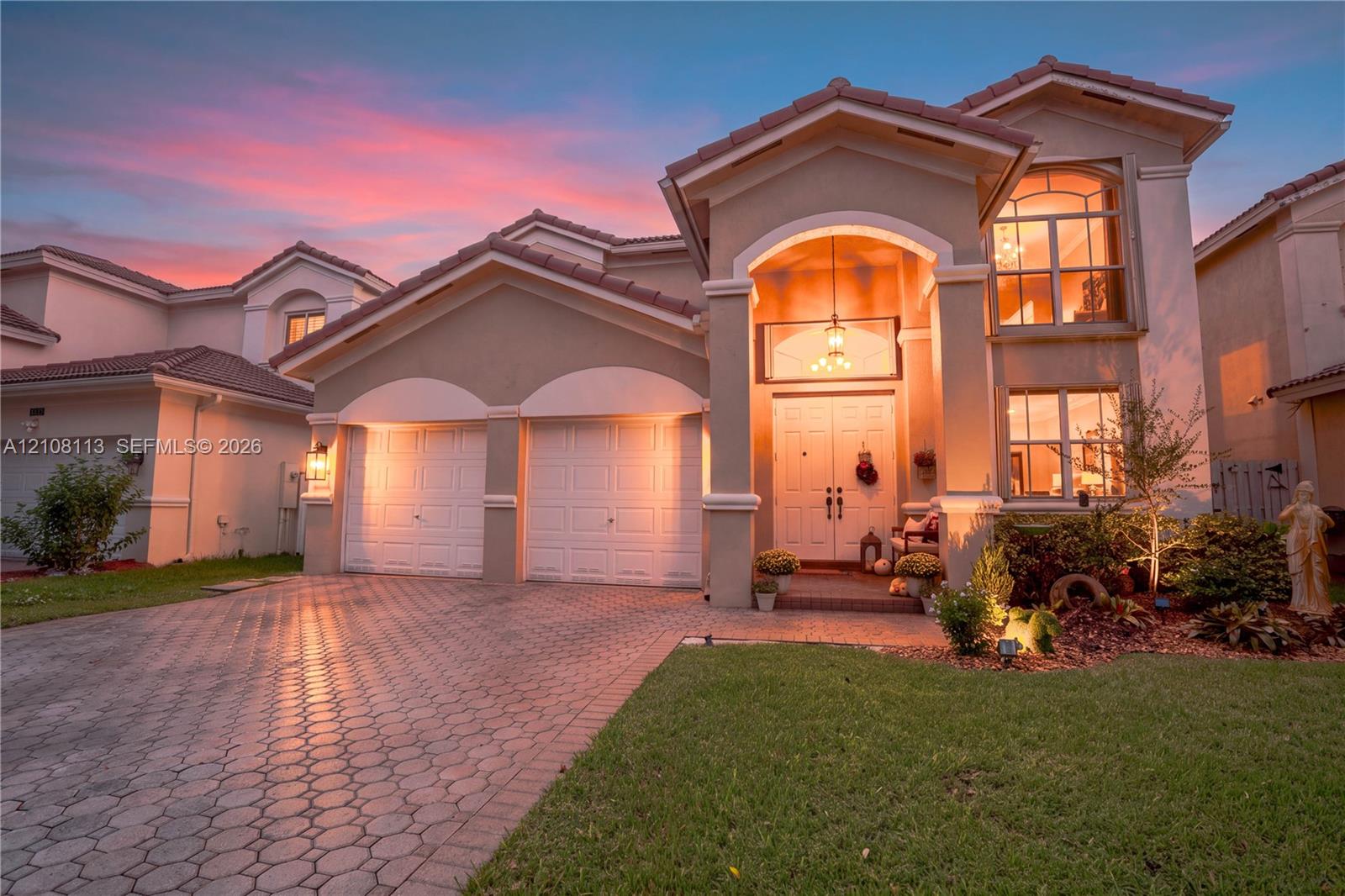 Stucco exterior featuring a dual-car garage, arched covered entryway, paver driveway, and tiled roof