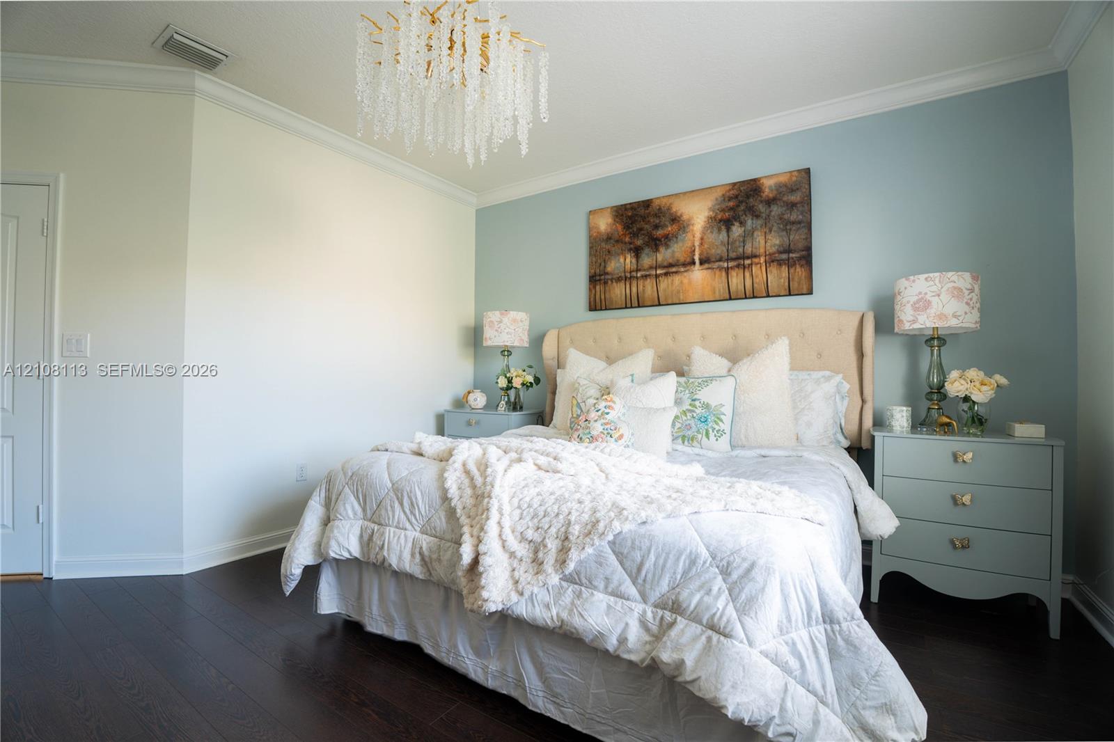 Room featuring dark wood-finish flooring, crown molding, and a tiered crystal chandelier