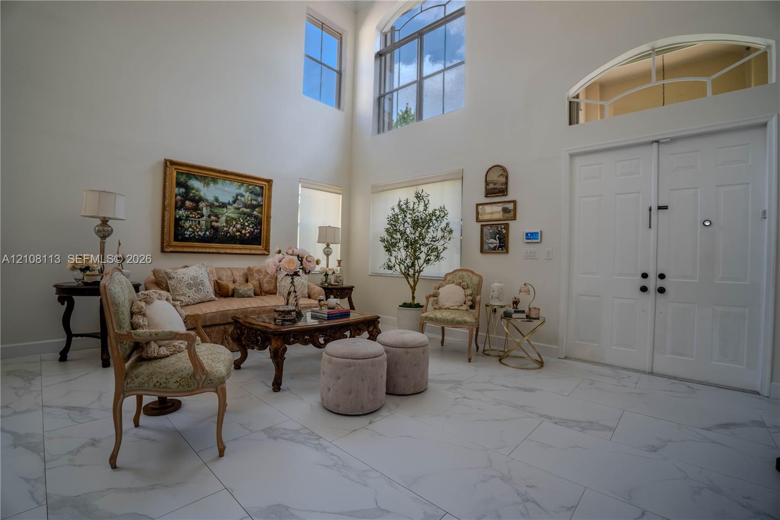 Double-height ceilings featuring expansive windows with an arched transom, double-door entry, and large-format tile flooring with marble-pattern veining