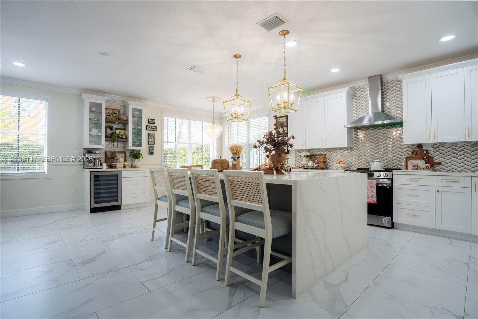 Kitchen featuring a central island with stone-finish waterfall edges, herringbone-patterned tile backsplash, white shaker-style cabinetry, stainless steel range hood, and porcelain tile flooring