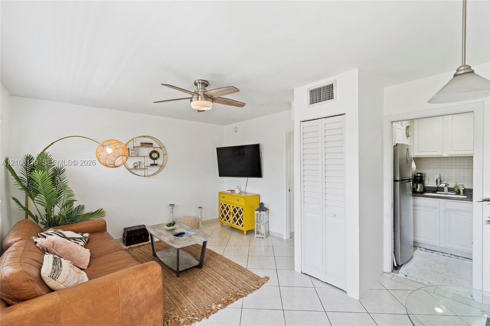Living area featuring neutral tile flooring, a multi-blade ceiling fan with integrated lighting, and a closet with louvered doors