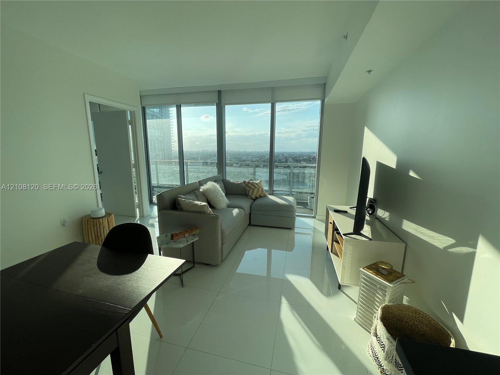 Floor-to-ceiling windows, high-gloss tile flooring, and a private balcony featuring a glass railing