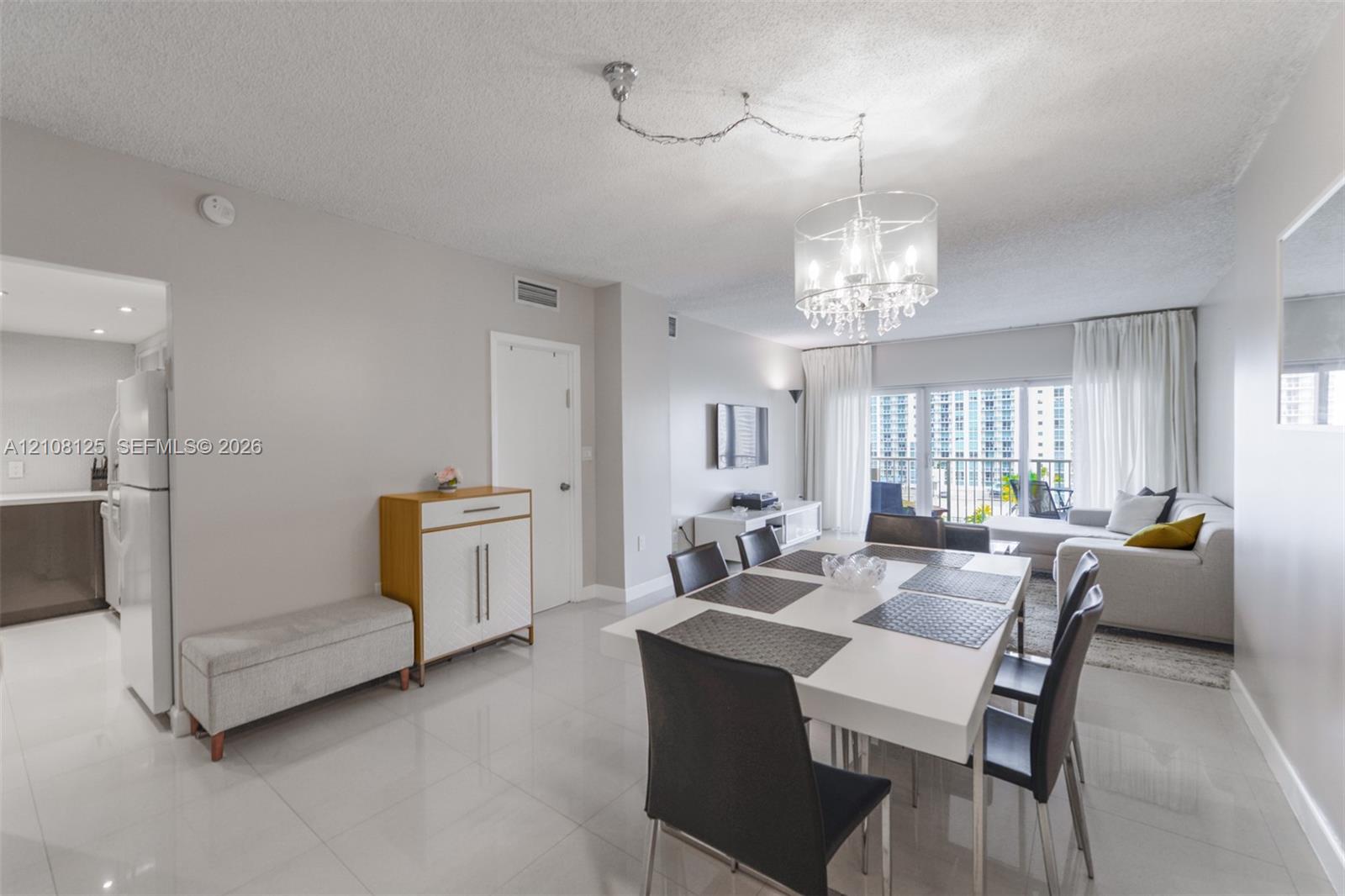 Open-concept living space featuring large-format tile flooring, a multi-light crystal chandelier, and floor-to-ceiling glass sliding doors providing natural light