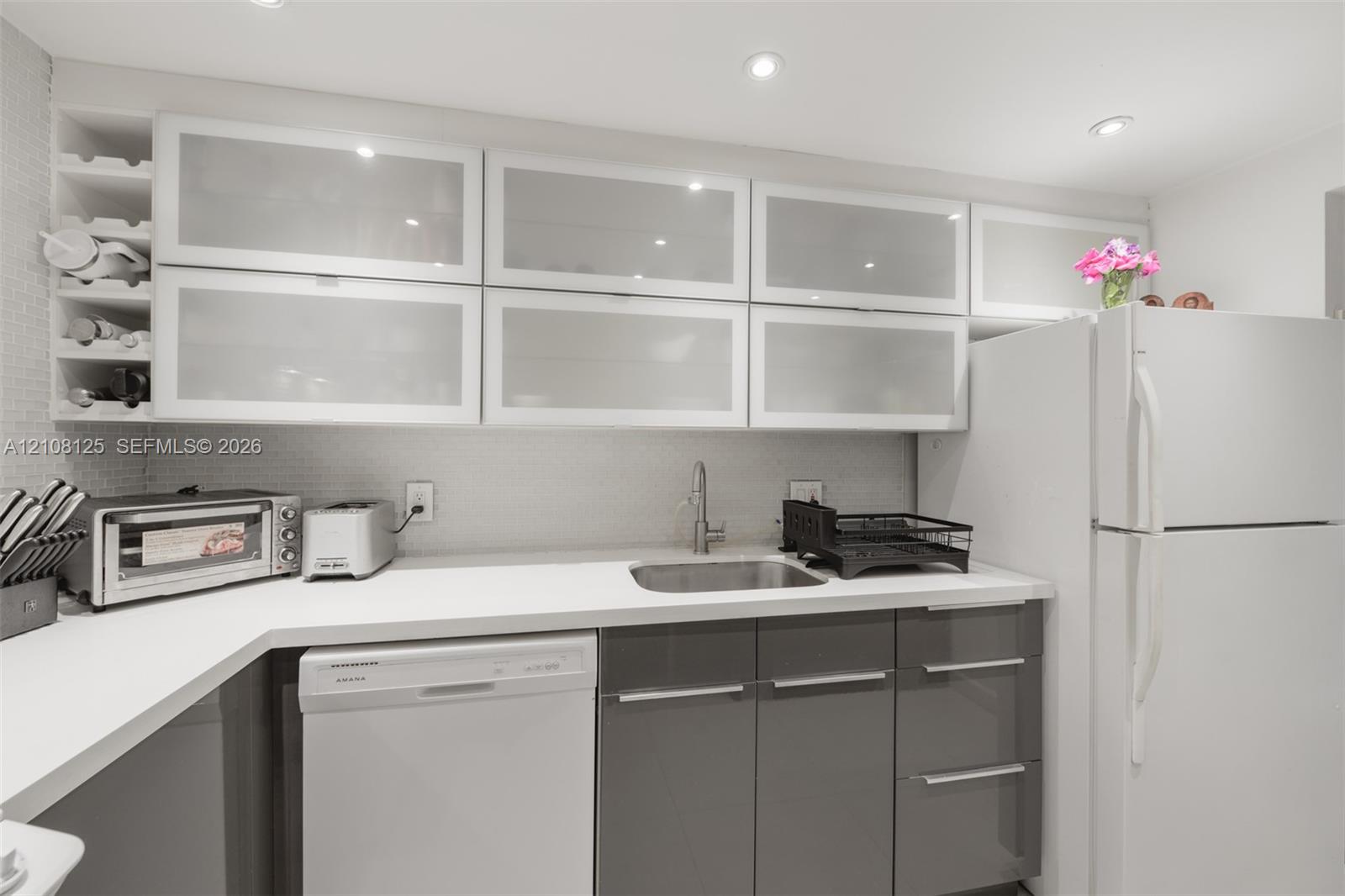 Kitchen featuring high-gloss charcoal base cabinetry, upper cabinets with frosted glass inserts, solid-surface countertops, recessed ceiling lighting, and integrated wine storage
