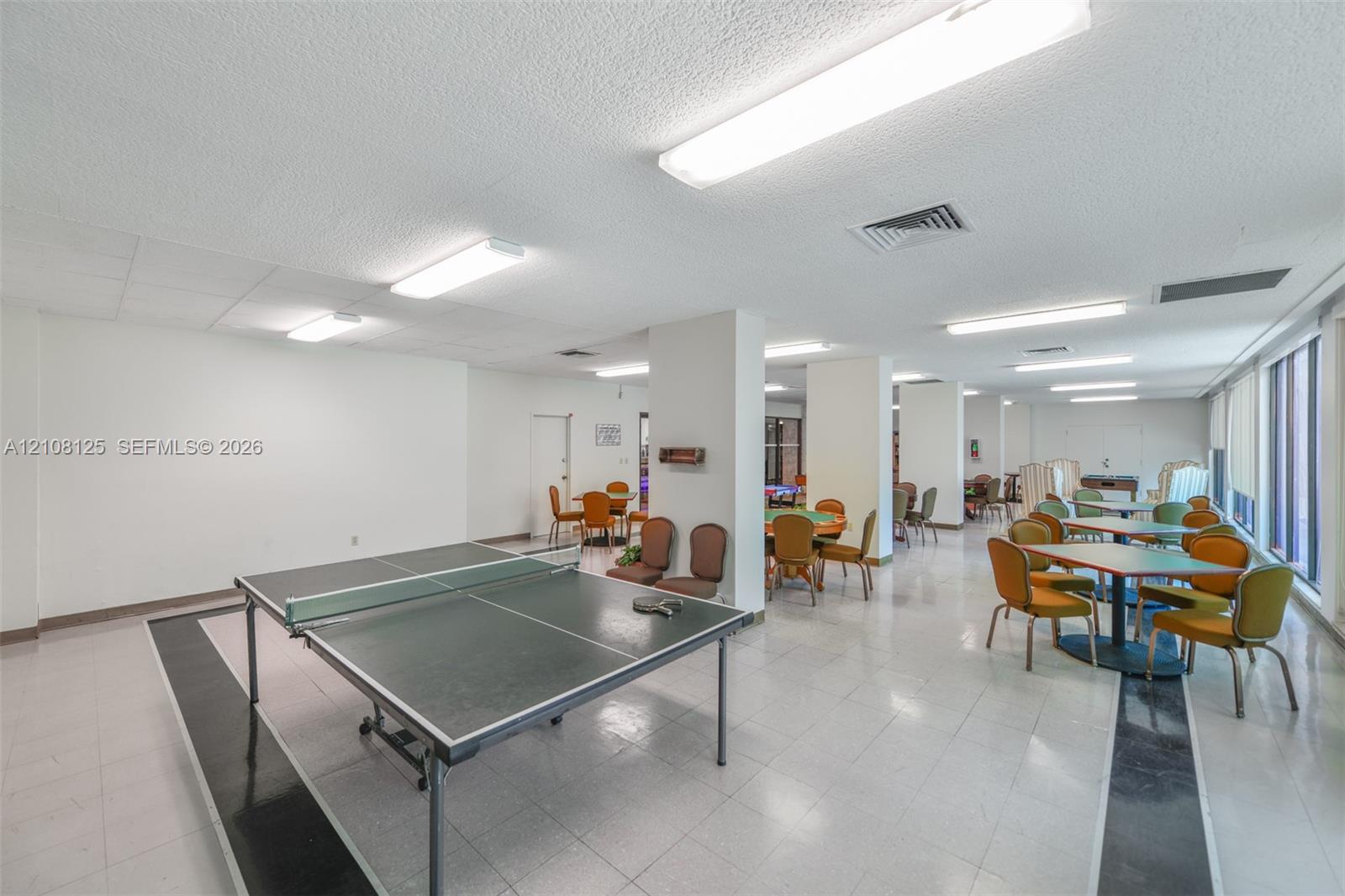 Open-concept interior space featuring ceramic tile flooring with decorative dark accents, structural support columns, and multiple flush-mount linear lighting fixtures
