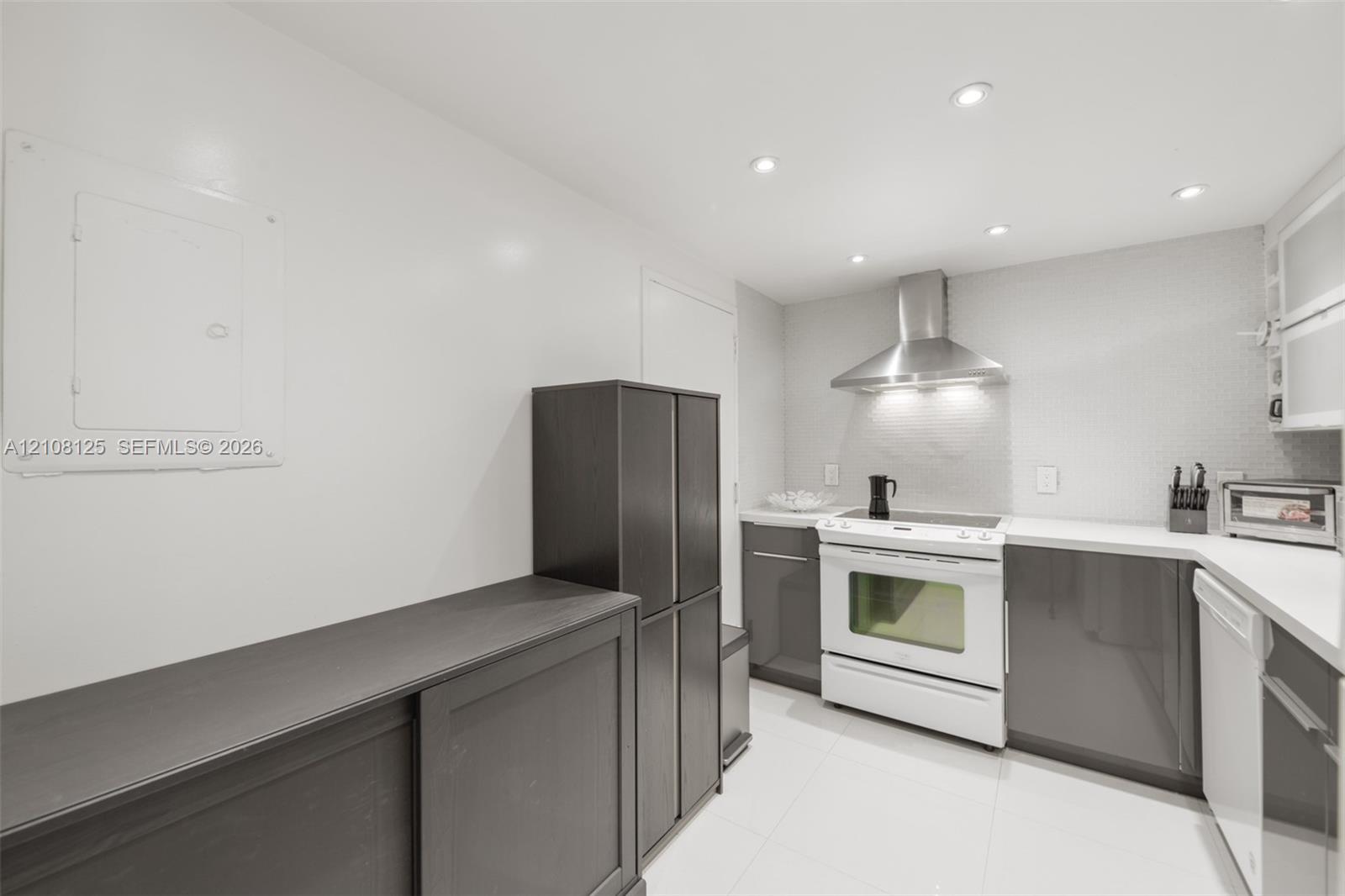Kitchen featuring dark-toned cabinetry, white countertops, stainless steel range hood, built-in range, and recessed ceiling lighting