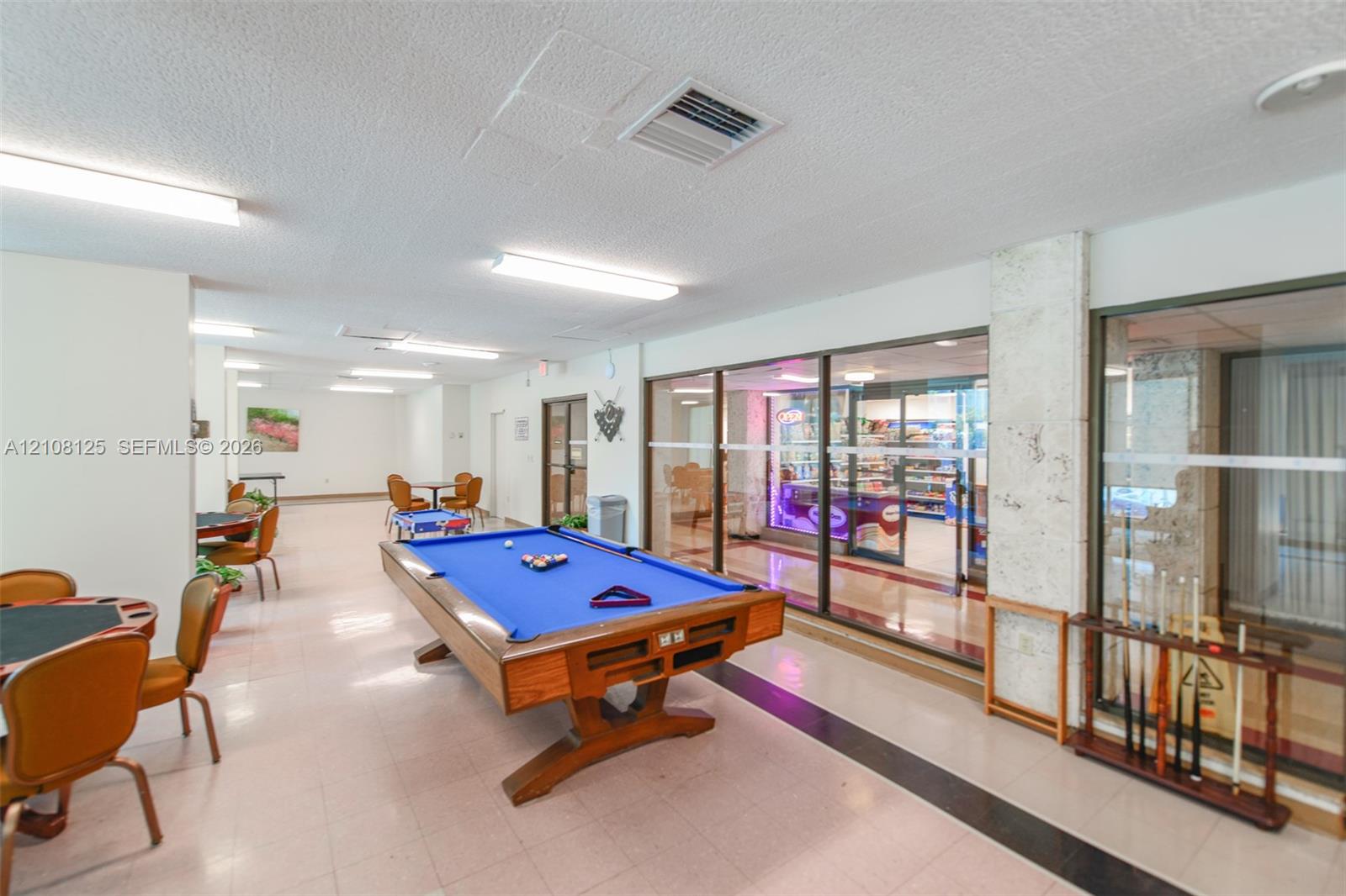Open-concept recreation space featuring ceramic tile flooring, linear overhead lighting, and expansive glass partition walls