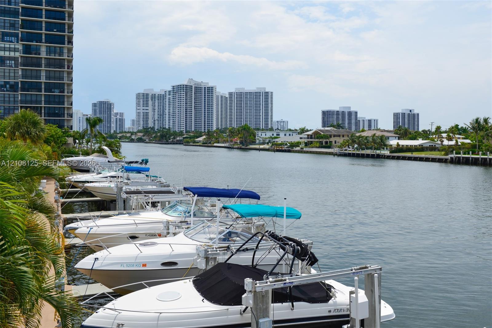 Waterfront canal setting featuring private boat slips, mechanical boat lifts, concrete seawall, and tropical landscaping