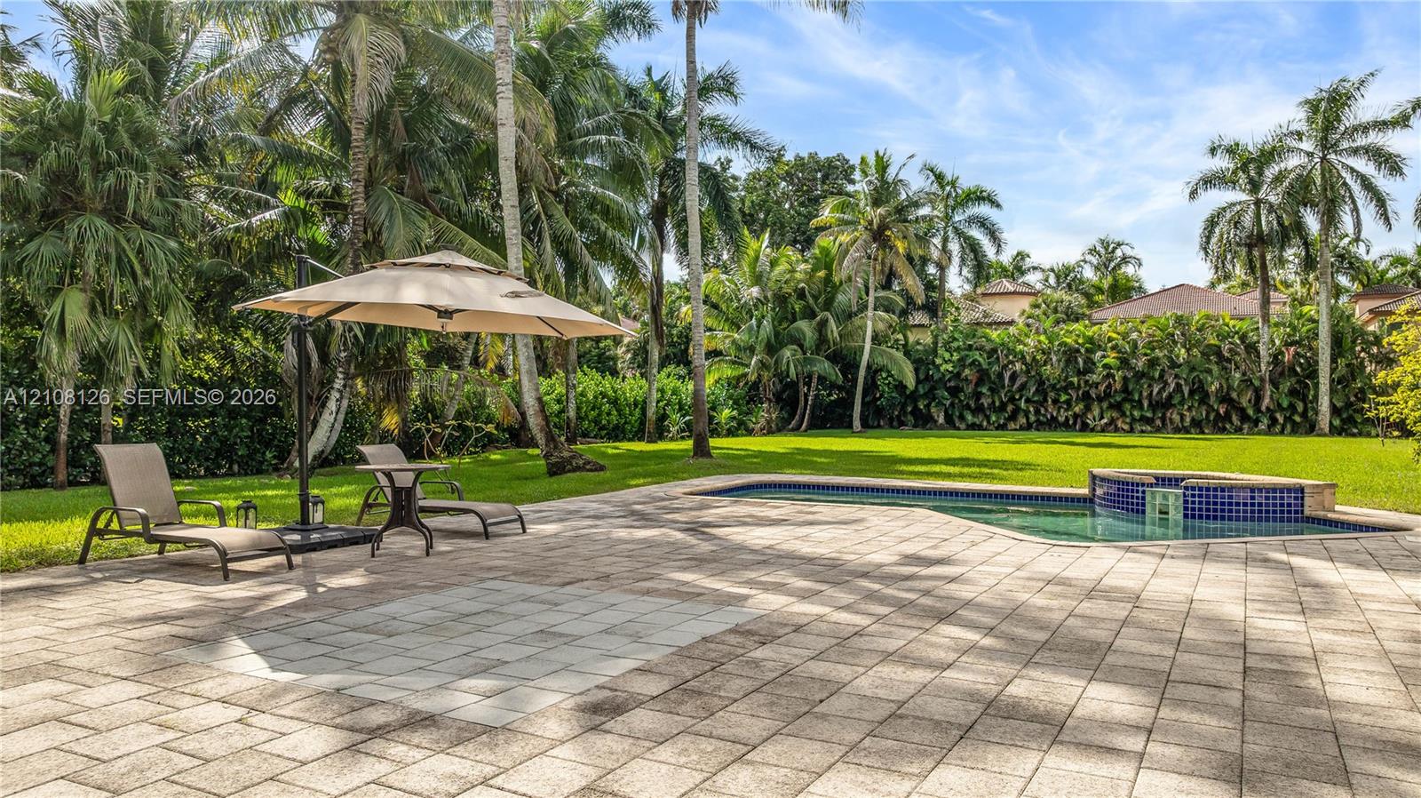 Expansive backyard featuring a stone-paver patio, swimming pool, raised tiled spa, manicured lawn, and mature palm trees