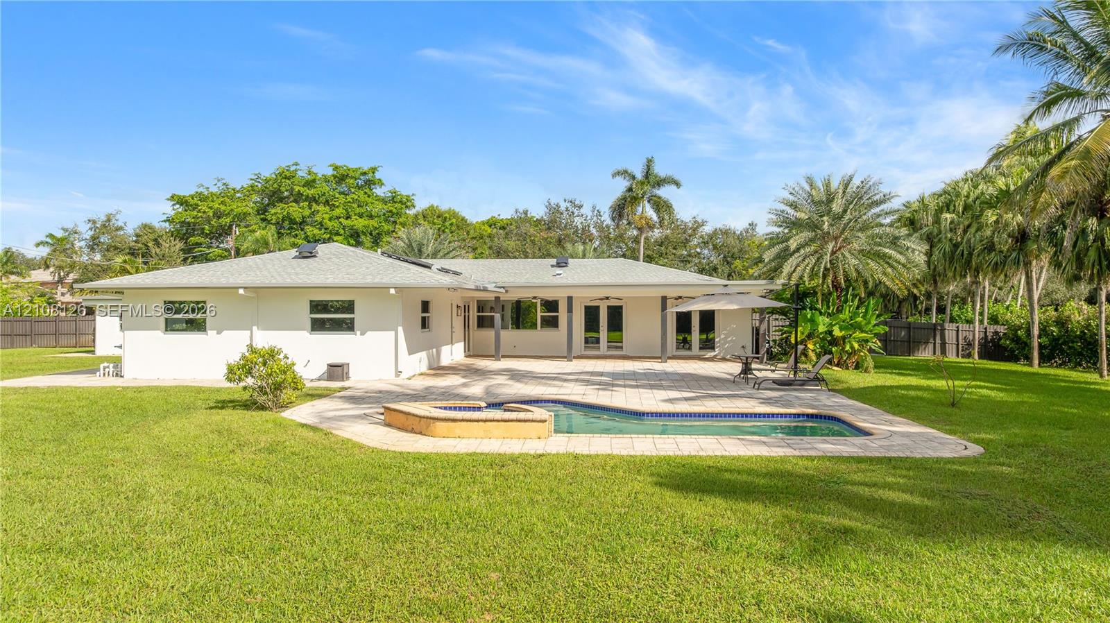 Rear exterior featuring a paver patio, in-ground pool with a raised stone-finish spillway, expansive grass lawn, and mature perimeter landscaping