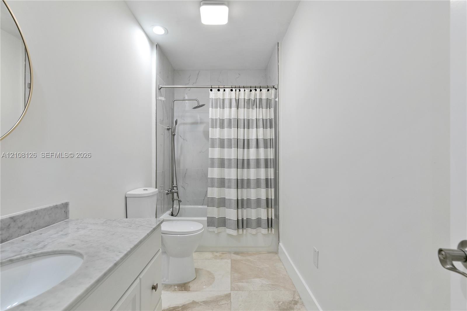 Bathroom featuring a vanity with a stone-top counter, undermount sink, shower-tub combination with stone-style surround, and tile flooring