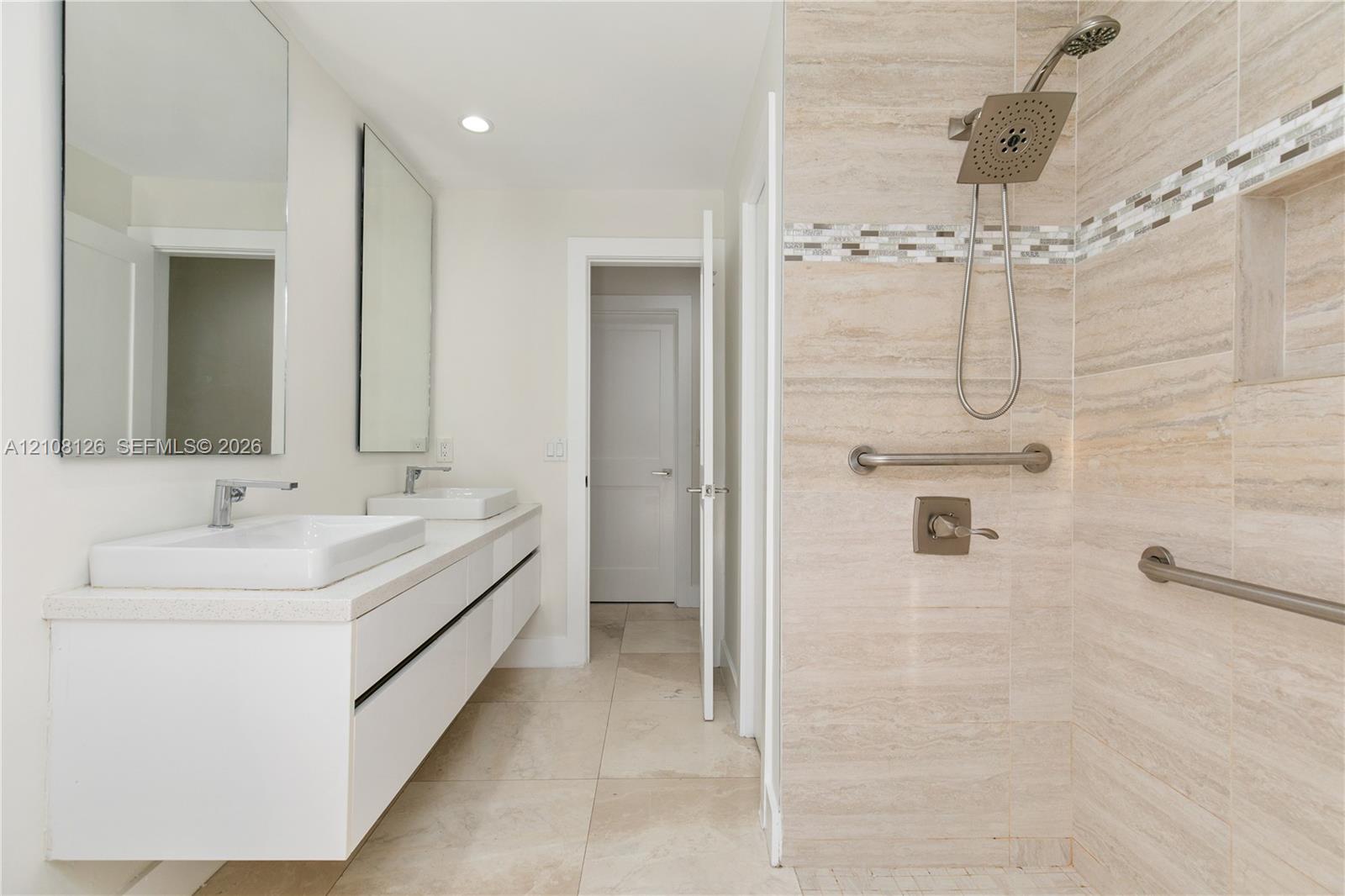 Floating vanity with dual rectangular vessel sinks, wall-mounted rectangular mirrors, walk-in shower with stone-finish tile surround, built-in shower niche, and metallic grab bars