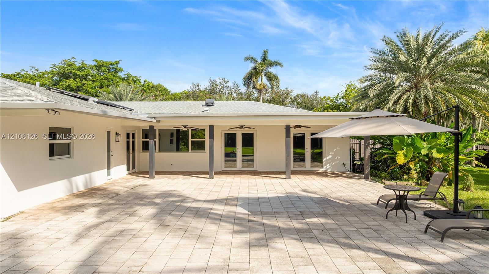 Expansive paver patio featuring a covered area with ceiling fans, dual French door entries, and mature landscaping