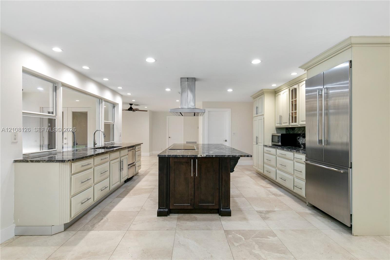 Kitchen featuring a central island with a stone countertop, custom cabinetry, stainless steel refrigerator, stone-tiled flooring, and recessed ceiling lighting