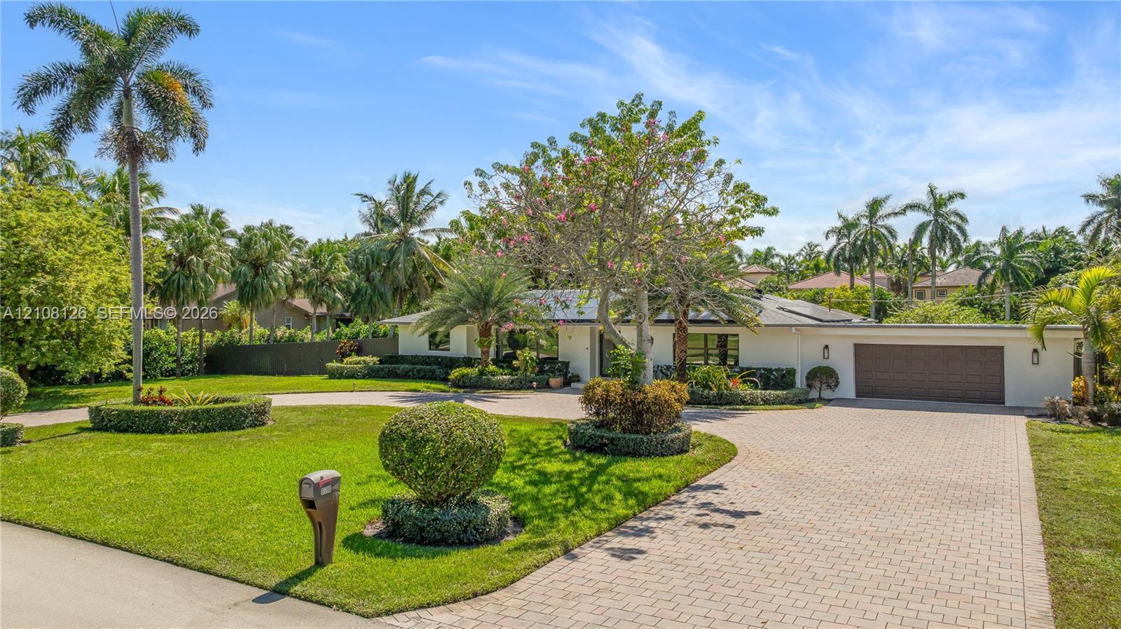 Single-story exterior featuring a paver driveway, an attached garage, and manicured landscaping with mature palm trees