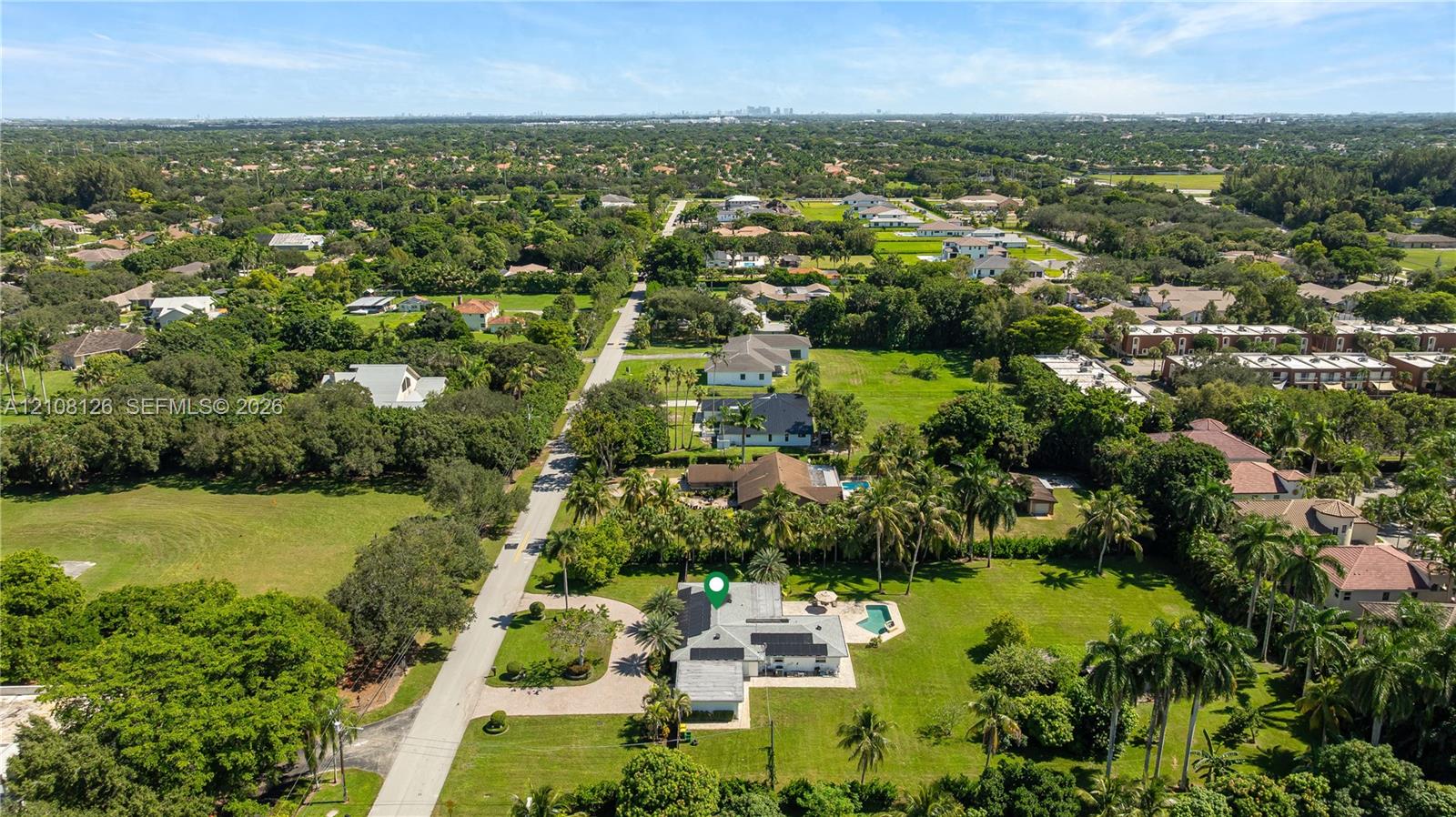 Aerial view of property featuring a circular paved driveway, expansive lawn, mature palm trees, and an in-ground swimming pool