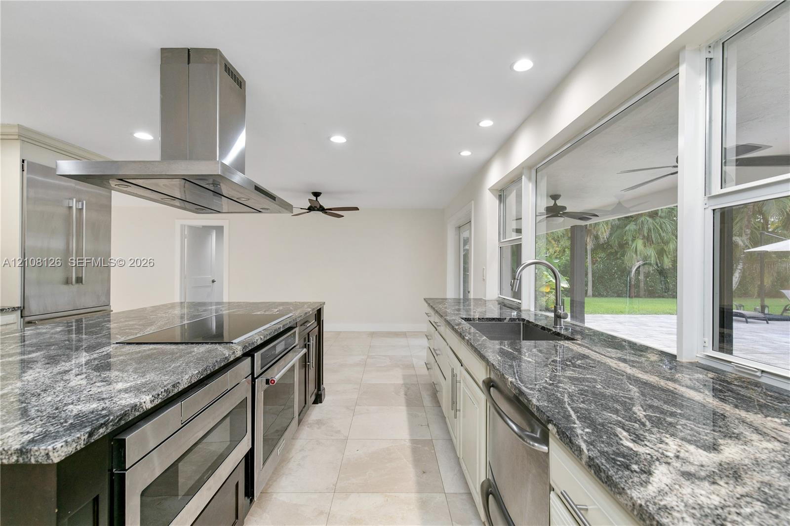 Kitchen featuring polished stone countertops, stainless steel appliances, a ceiling-mounted range hood, light-toned tile flooring, and large windows