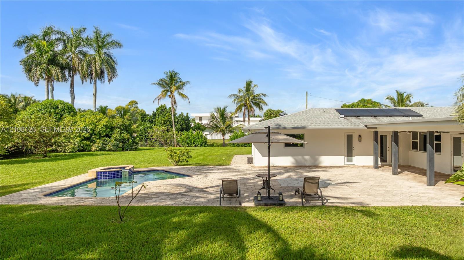 Expansive backyard featuring a stone-paved patio, custom swimming pool with built-in spa, solar panel roof installation, and mature landscaping