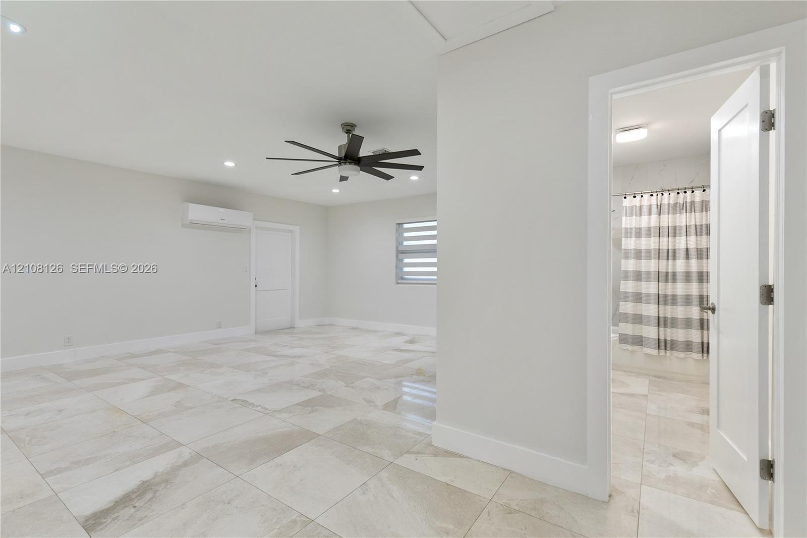 Large-format tile flooring, multi-blade ceiling fan, recessed lighting, wall-mounted air conditioning unit, and dual-pane window