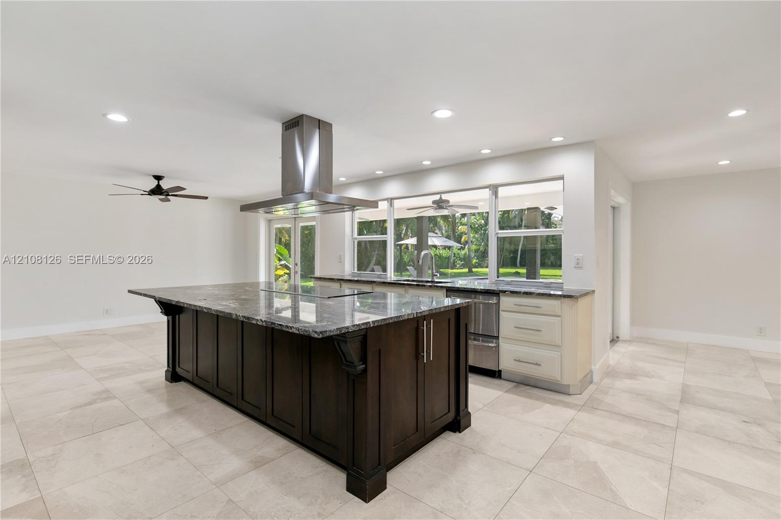 Kitchen featuring a large central island with dark cabinetry, stone-finish countertops, stainless steel professional-grade range hood, recessed lighting, and large-format tile flooring