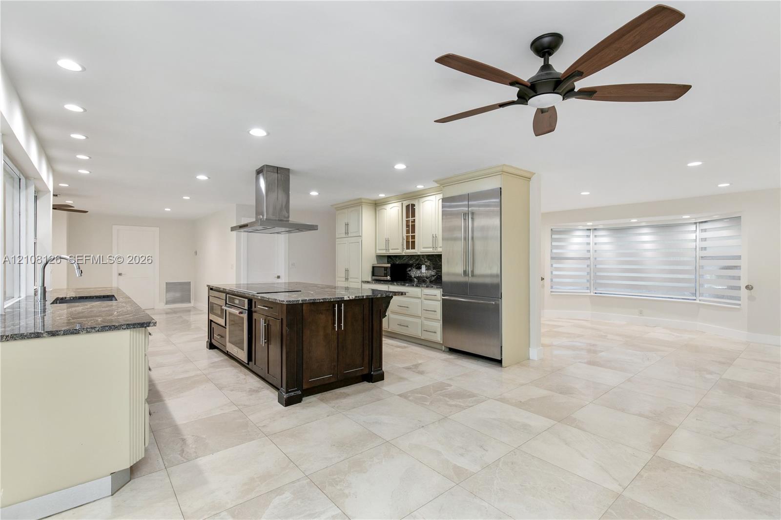 Kitchen featuring a center island with dark wood-finish cabinetry, stainless steel appliances, a stainless steel range hood, stone countertops, and tile flooring