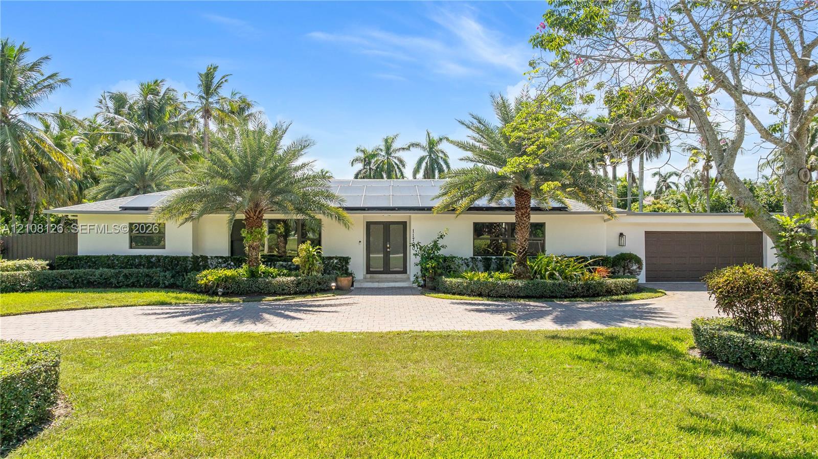 Single-story residence featuring a paved circular driveway, solar panel array, attached multi-car garage, and established landscape