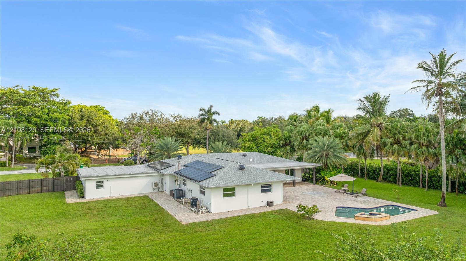 Expansive backyard featuring a paver patio, in-ground pool with a spillover spa, solar panel array, and mature landscaping