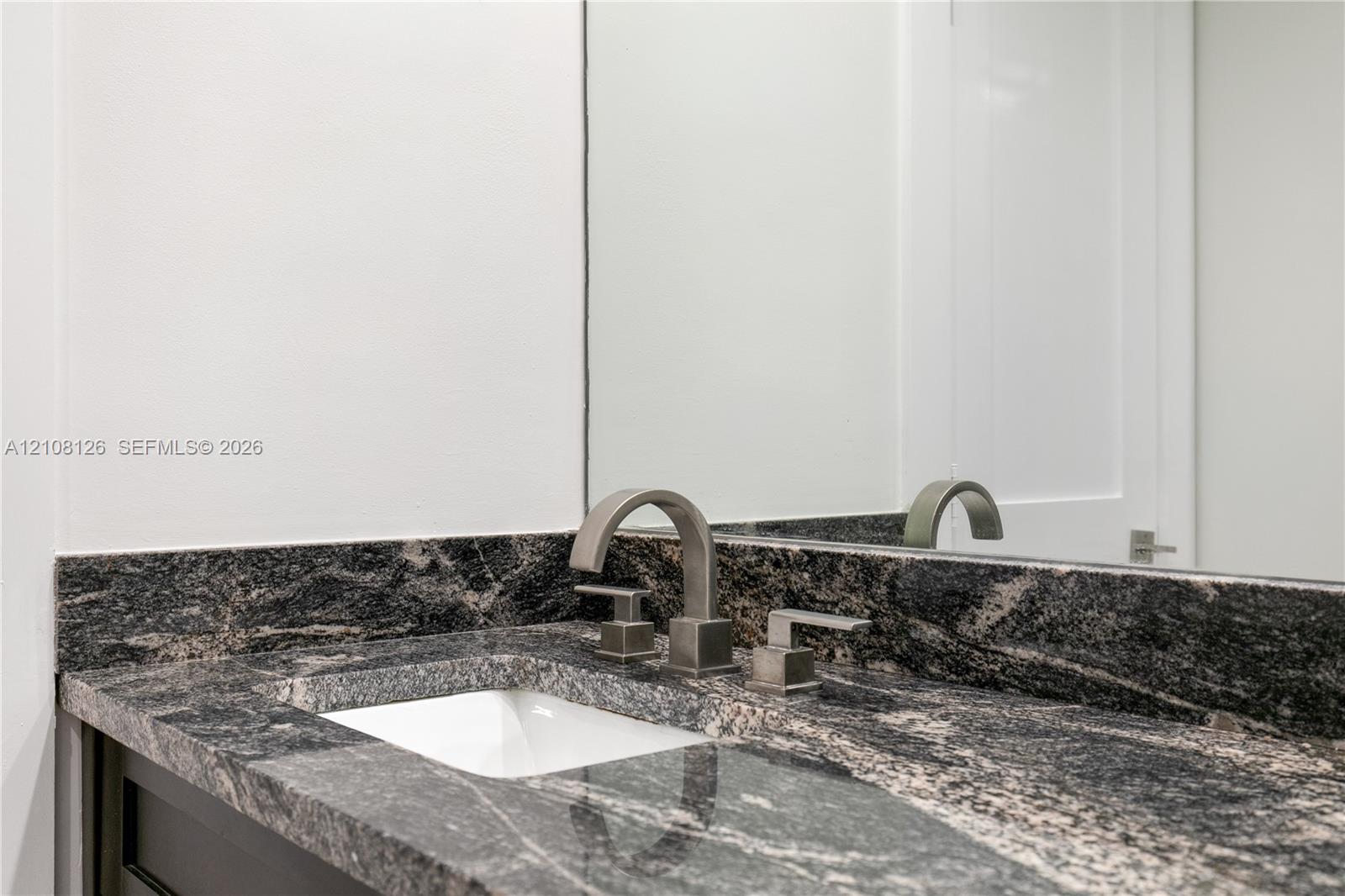 Stone countertop with integrated backsplash, under-mount basin, and metallic widespread faucet, complemented by a wall-mounted mirror