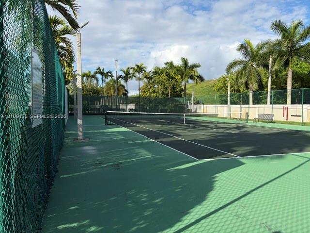 Tennis court with a multi-colored hard surface, perimeter chain-link fencing, and surrounding palm trees