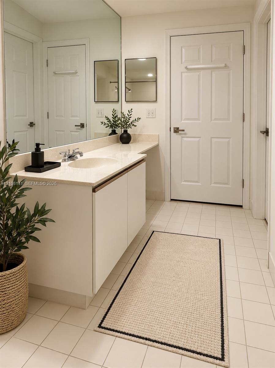 Bathroom vanity featuring a solid surface countertop, an integrated sink, flat-panel cabinetry, a full-width wall mirror, and ceramic tile flooring