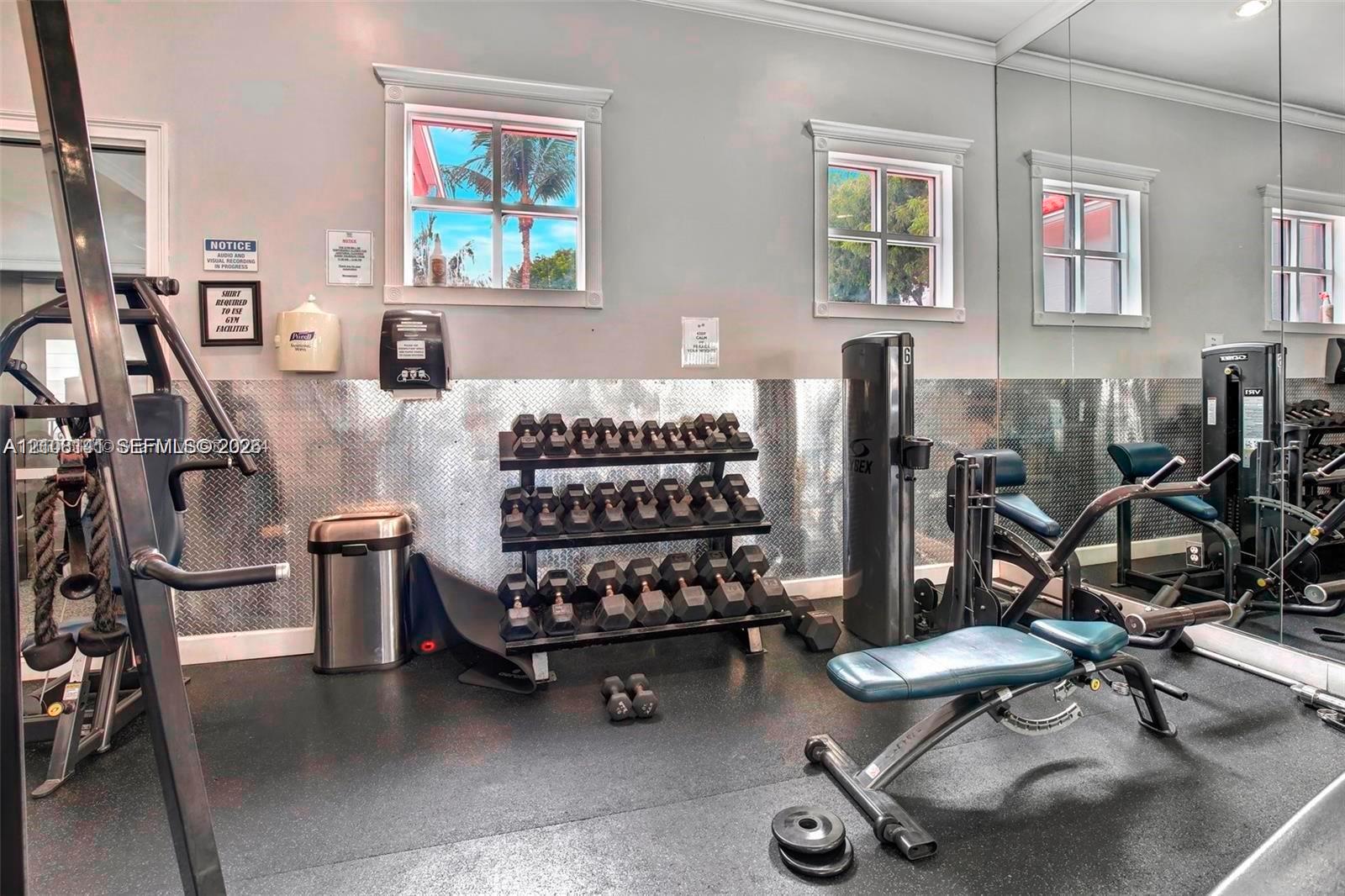 Fitness space featuring rubber flooring, floor-to-ceiling mirrored walls, diamond-plate metal wall paneling, and multi-pane windows with trim casing