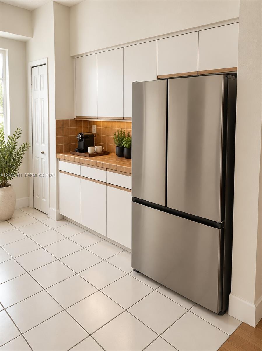 Kitchen area featuring white flat-panel cabinetry, a stainless steel French door refrigerator, tiled backsplash, and ceramic tile flooring