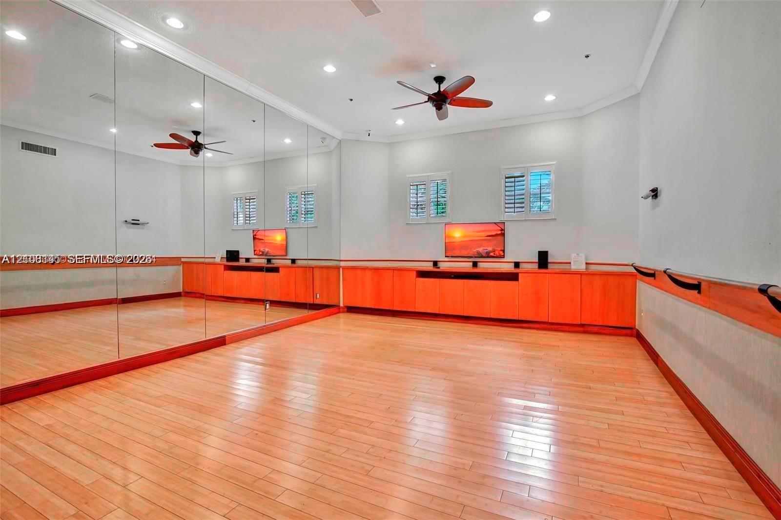 Full-length wall mirrors, light wood-finish flooring, custom built-in wood cabinetry, recessed lighting, and a wall-mounted ballet barre