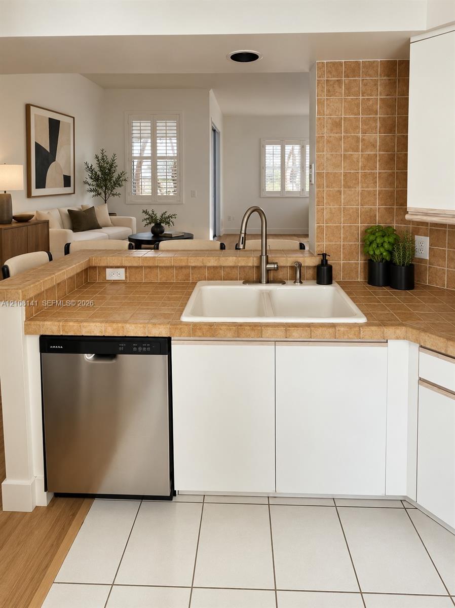 Kitchen area featuring a stainless steel dishwasher, white cabinetry, tiled countertops and backsplash, and a dual-basin sink with a gooseneck faucet