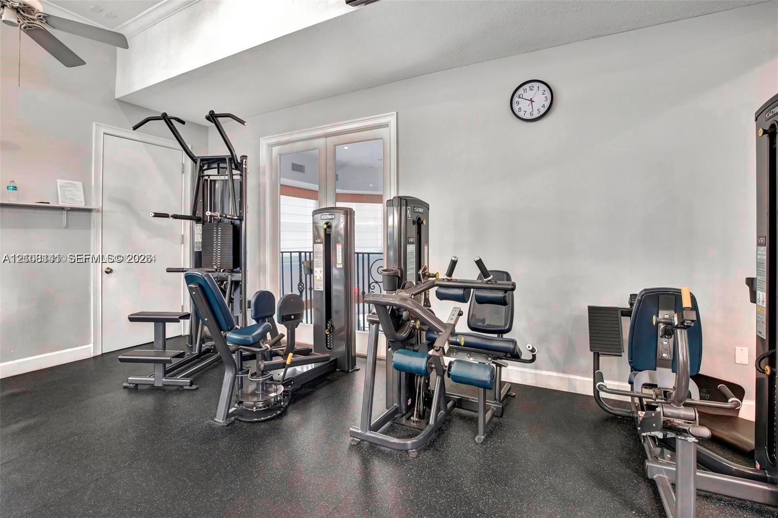 High ceiling featuring a flush-mount ceiling fan, double glass-panel doors with decorative metal railing, and resilient rubber-finish flooring