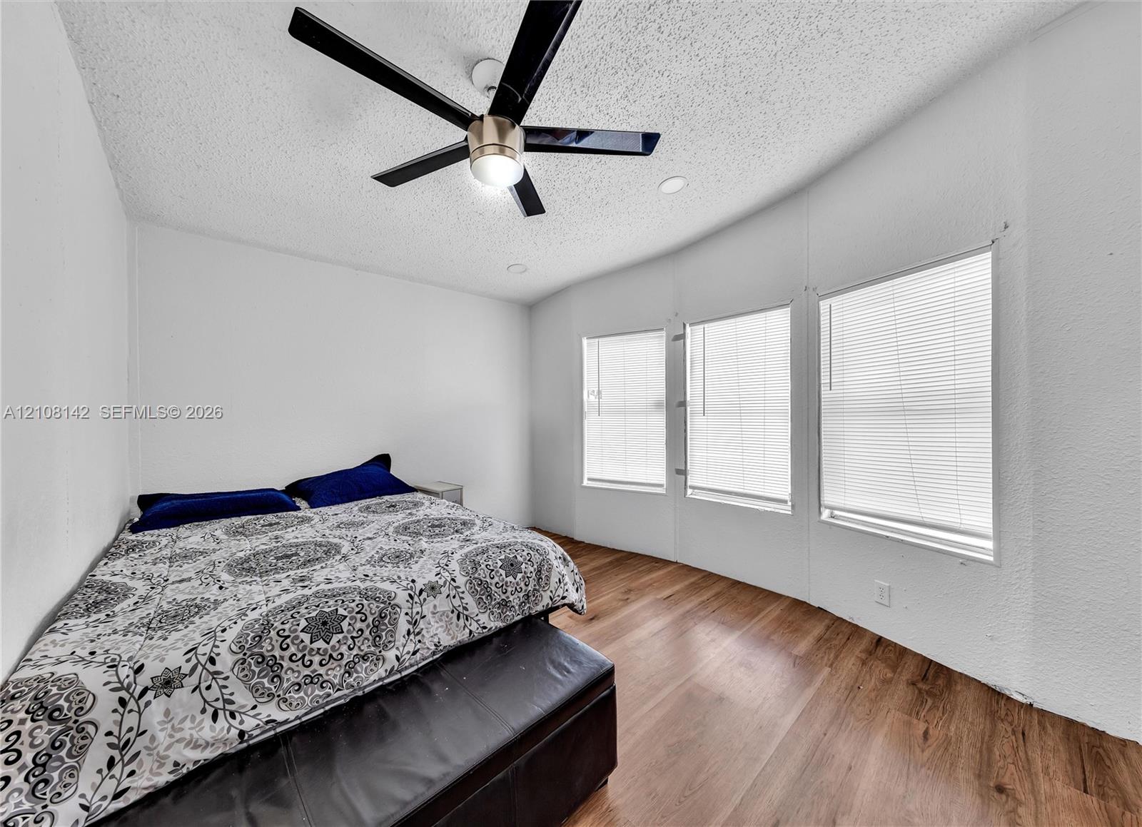 Wood-finish flooring, three large windows, and a matte black ceiling fan with integrated lighting