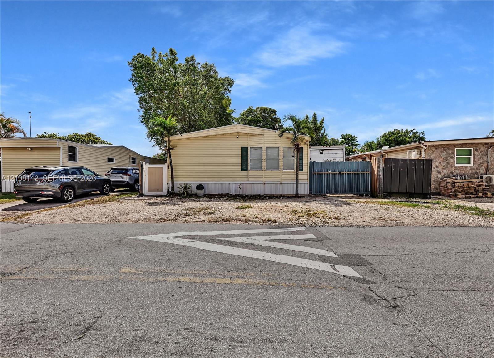 Exterior featuring light-colored horizontal siding, dual palm trees, and gravel ground cover