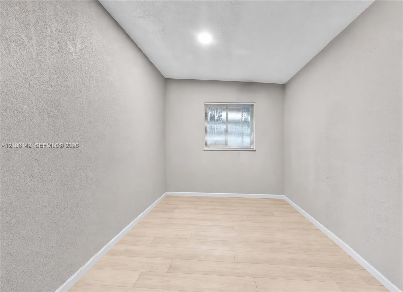 Neutral-toned interior space featuring wood-finish flooring, recessed lighting, and a window with integrated blinds