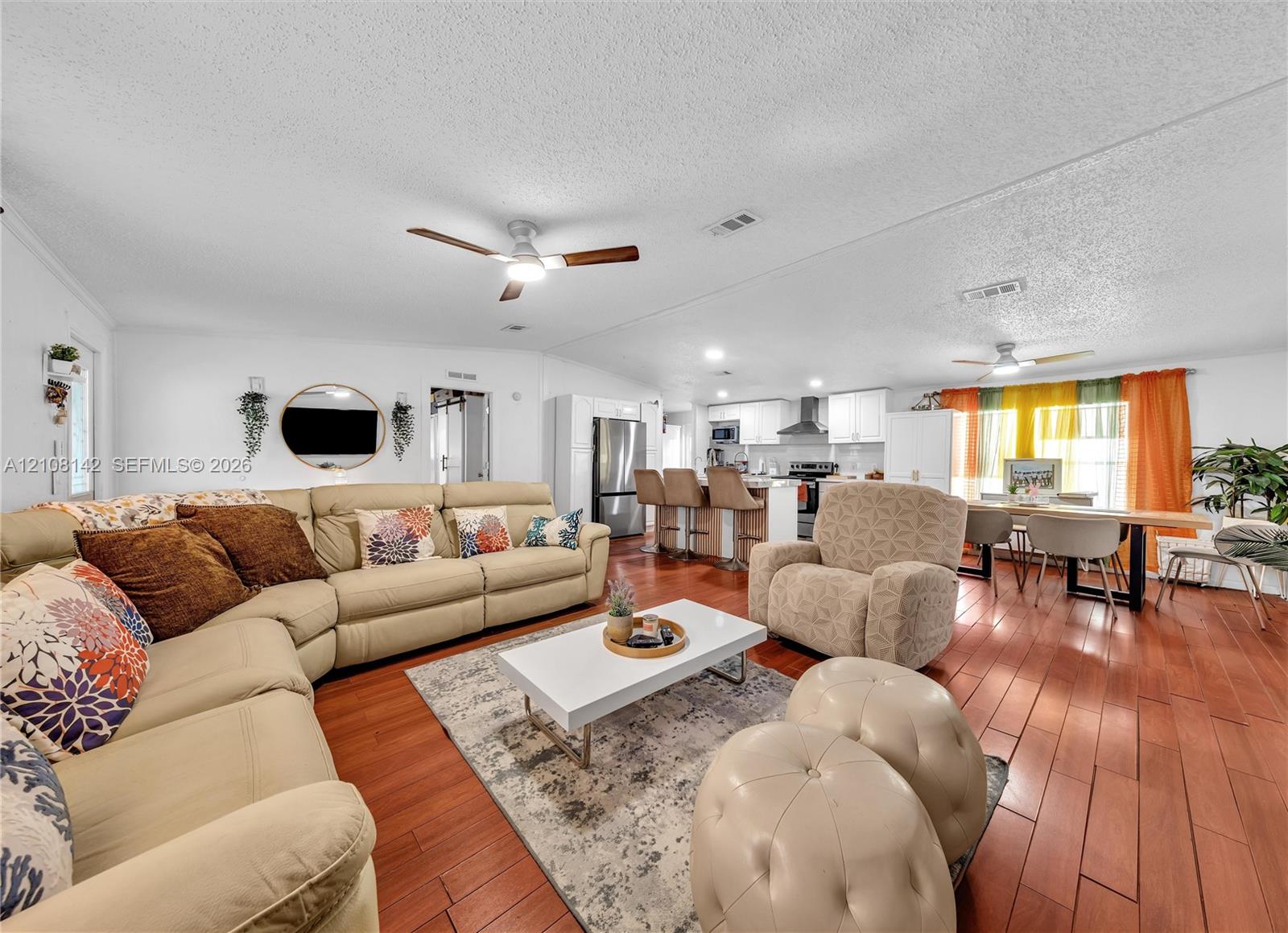 Open-concept floor plan with wood-finish flooring, recessed lighting, ceiling fans, and a kitchen featuring white cabinetry and a stainless steel refrigerator