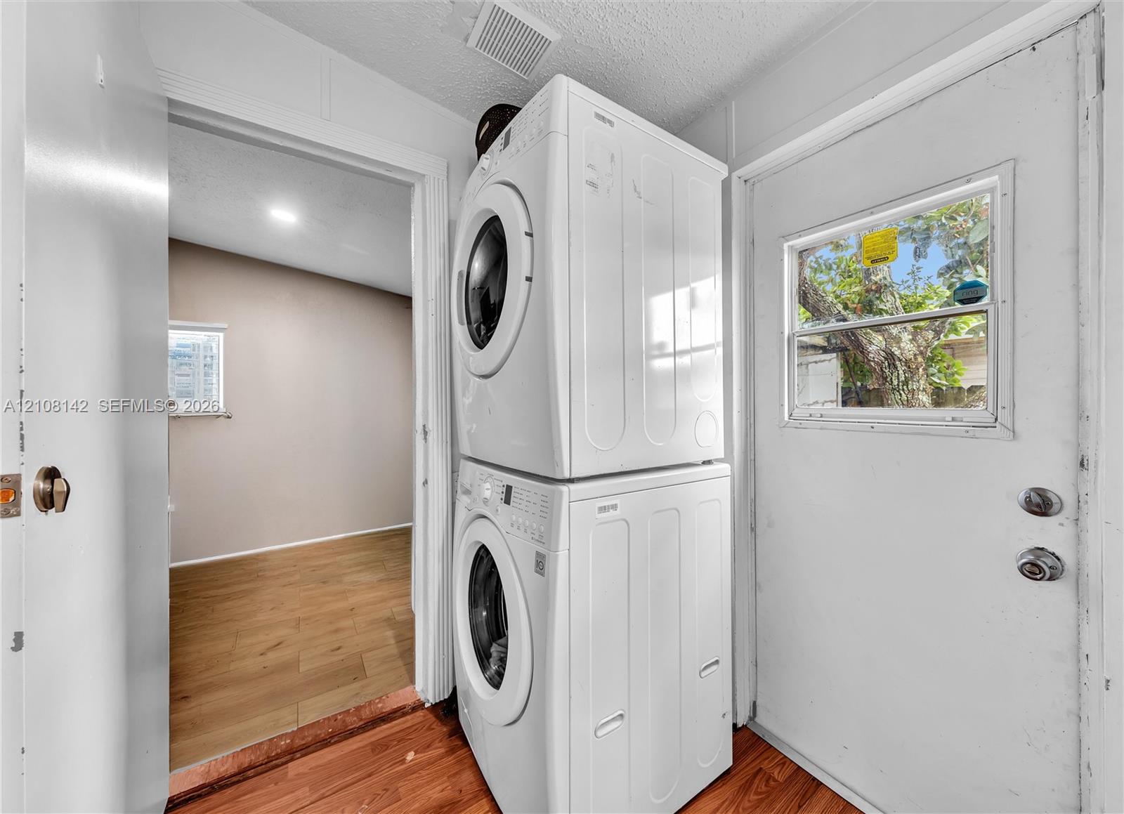 Utility area featuring a stacked washer and dryer unit, wood-finish flooring, and a door with an inset window