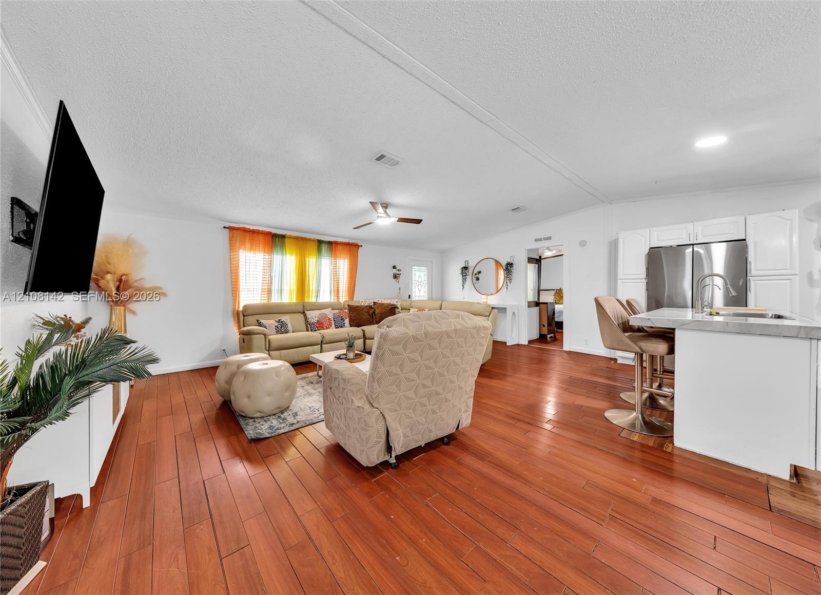 Open-concept interior featuring wood-finish flooring, a kitchen island with stone-finish countertops, stainless steel appliances, white cabinetry, and a ceiling fan