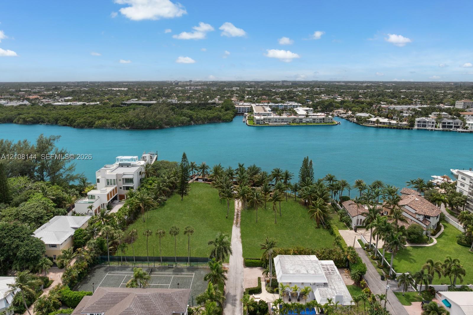 Waterfront parcel featuring extensive lawn, established palm trees, and a hard-surfaced tennis court
