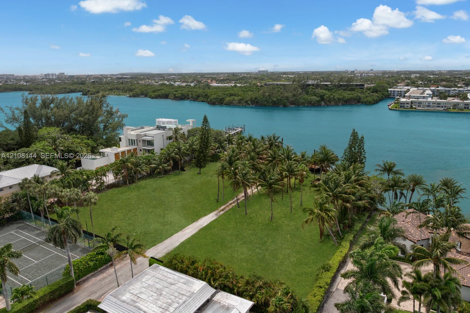 Waterfront parcel featuring extensive lawn space, established palm trees, a private tennis court, and direct shoreline access