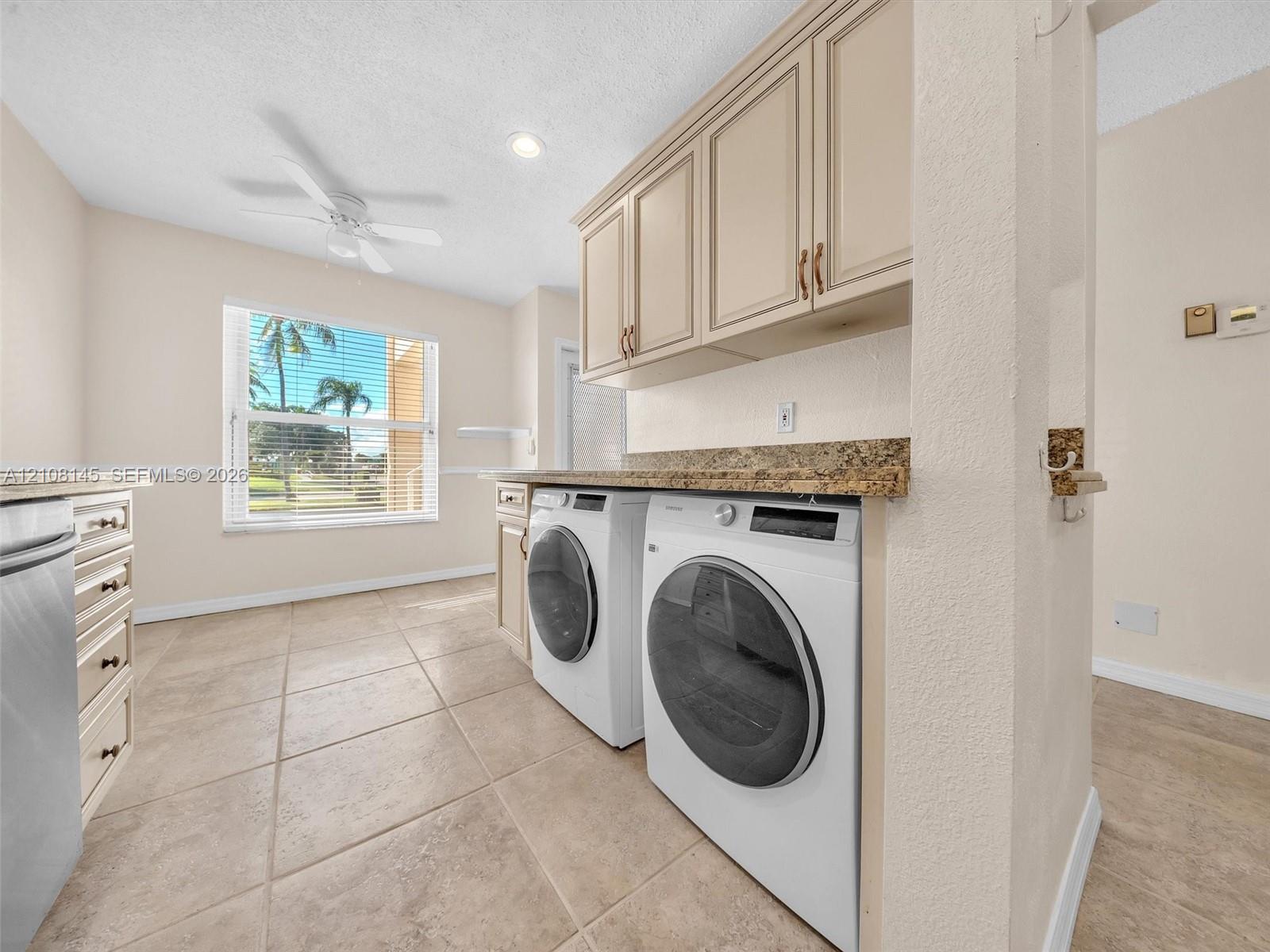Laundry area featuring stone-finish countertops, wall-mounted cabinetry, tile flooring, a ceiling fan, and a window with exterior scenery
